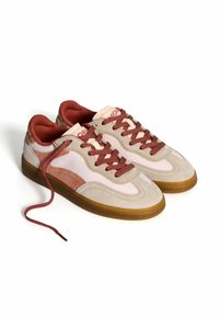 Zapatillas con una parte superior de ante beige suave, acentos en rosa claro, cordones rojos y una suela de goma marrón. Punta redondeada y detalle de cuello acolchado.