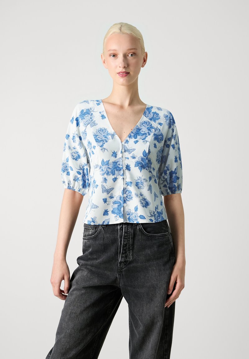 Blå bluse med blomstermønster, V-hals, korte puffærmer og knaplukning, parret med mørkegrå jeans. Let stof og afslappet pasform.