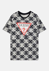 Camiseta blanca con el logotipo "GUESS" en negro y rojo, presentado en un patrón gráfico repetido con signos de interrogación; mangas cortas y escote redondo.