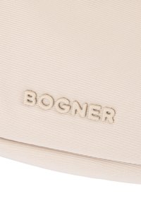Bolso de color crema con superficie de tela texturizada y logo "BOGNER" en relieve. Diseño elegante con bordes sin costuras para un aspecto moderno.