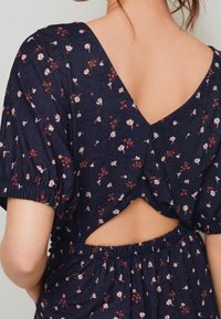 Květinové námořnické šaty s hlubokým V-výstřihem na zádech, zvonovými rukávy a elastickým pasem. Obsahují malé bílé a červené květinové vzory po celém povrchu.