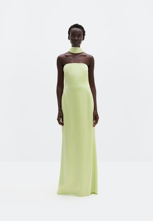 Naine seisab valgel taustal, vaatega ettepoole, kandes rihmadeta, põrandapikkust helerohelist kleiti koos sobiva kaelus salliga.