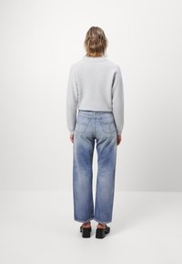 Světle šedý svetr přes modré volné džíny s vybledlým omakem. Džíny mají zadní kapsy a jemné švy, zakončené surovým lemem.