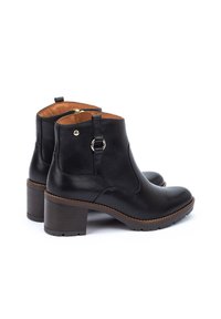 Bottines en cuir noir à bout arrondi, avec un petit talon carré et des coutures brunes. Elles présentent une boucle sur le côté et des éléments en métal doré.