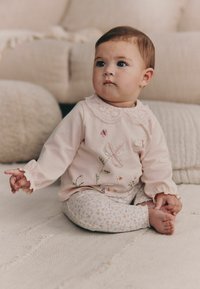 Camisa de manga larga rosa claro con un cuello de encaje, adornada con mariposas y flores bordadas; combinada con leggings estampados con motivos florales.
