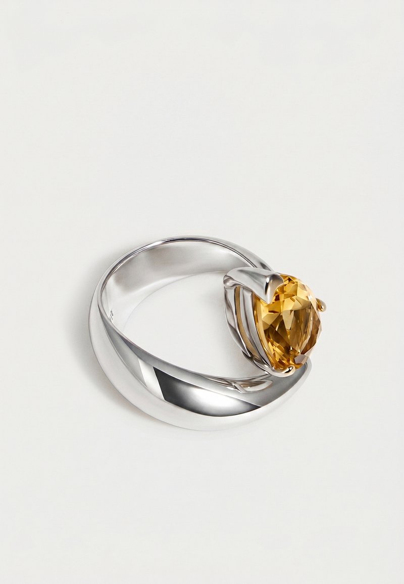 Anillo de plata con diseño de banda torcida que sostiene una gran piedra preciosa oval amarilla en un engaste de garras sobre fondo blanco.