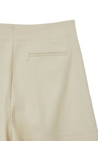 Pantaloni in tessuto beige con una tasca welt singola sul retro e cuciture a vista.