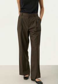 Bruine, breed-gesneden broek met een gestructureerde afwerking, voorzien van voorkeurs-plooien en zijzakken. Gecombineerd met een zwart mouwloos topje en zwarte flats.