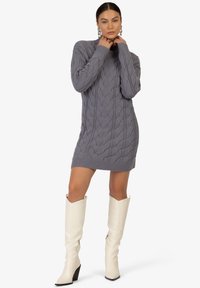 Abito maglione grigio a maglia con motivo a trecce, orlo a costine e colletto alto, abbinato a stivali bianchi in pelle fino al ginocchio con tacco quadrato.