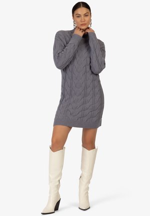 Graues gestricktes Sweaterkleid mit Kabelmuster, geripptem Saum und hohem Kragen, kombiniert mit kniehohen weißen Lederstiefeln mit Blockabsatz.
