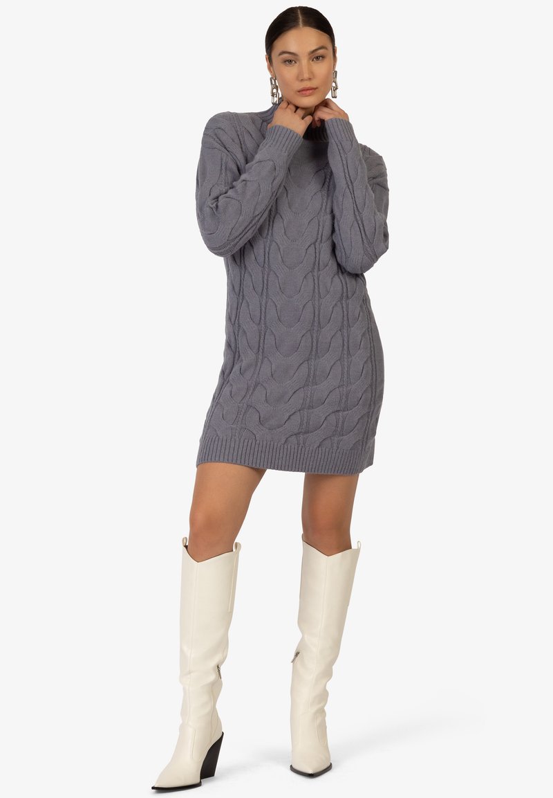 Abito maglione grigio a maglia con motivo a trecce, orlo a costine e colletto alto, abbinato a stivali bianchi in pelle fino al ginocchio con tacco quadrato.