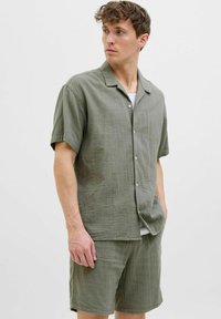 Olivengrøn kortærmet skjorte i struktureret stof med knaplukning og en afslappet pasform, parret med matchende shorts i samme materiale.