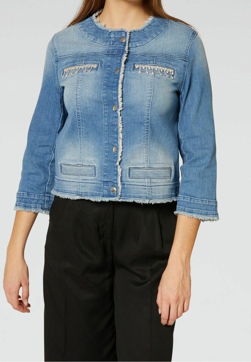 Blå denimjacka med kort design, fransiga kanter, två fickor fram och dekorativa sömmar på bröstet. Har metallknappar.