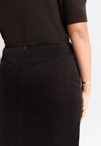 Black corduroy skirt with a fitted shape, featuring vertical ribbed texture and a subtle zipper at the back.