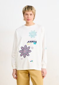Langermet hvit T-skjorte med grafiske blomsterdesign i rosa, blå og svart, med tekst-elementer og rund hals. Laget av bomull.