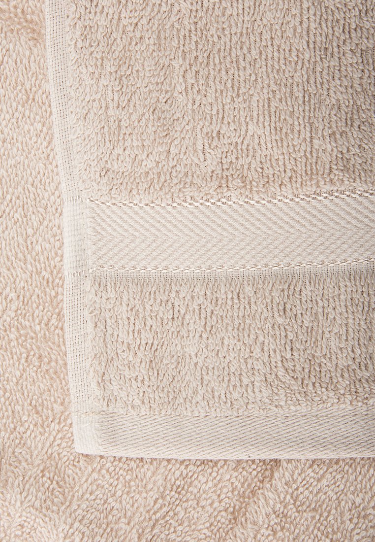 Beige Badetuch mit einer strukturierten Oberfläche und einem glatten, breiten Rand, der ein dezentes diagonales Muster zeigt. Weiches, saugfähiges Material.
