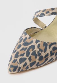 Flat παπούτσι με σχέδιο λεοπάρ, με μυτερή μύτη, φτιαγμένο από υφασμάτινη επιφάνεια σε μπεζ και σκούρο μπλε χρώμα, και έναν λεπτό ιμάντα στον αστράγαλο.