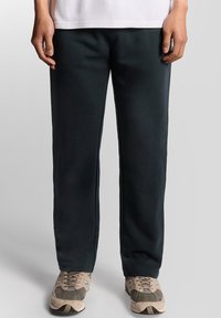 Mörkgröna sweatpants i mjuk tyg med avslappnad passform. Har sid sömmar och öppna fållar; matchas med beiga sneakers.