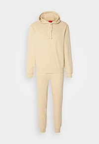 Sweat à capuche beige avec cordons et pantalon de jogging fuselé assorti, tous deux avec poignets et taille côtelés, ensemble de vêtements décontractés.