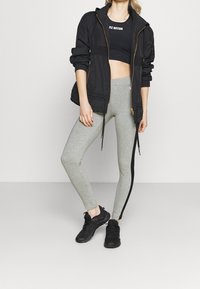 Giacca nera con zip sopra un top corto nero, abbinata a leggings grigi con una striscia laterale nera e scarpe da ginnastica nere.