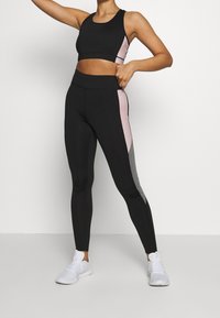 Svart sportig crop top med rosa sidpanelen; svarta leggings med grå och rosa siddekor; bärs med vita träningsskor.