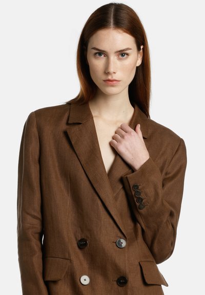 Blazer beige en lin à double boutonnage avec revers crantés, poignets à quatre boutons et poches avant. Texture lisse et coupe ajustée.