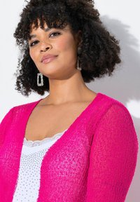 Fuchsia stickad cardigan med V-ringning, bärs över en vit topp med spetskanter och rhinstenar. Texturerad tyg.