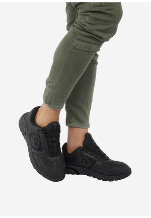 Schwarze Sportschuhe aus strukturiertem Mesh mit Gummiophälsen, ausgestattet mit Schnürsenkeln und dezentem Branding, kombiniert mit olivgrünen kurzen Hosen.