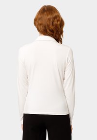 Camicia a maniche lunghe con colletto in morbido tessuto bianco. Texture liscia con una vestibilità su misura. Completa i pantaloni neri mostrati in basso.
