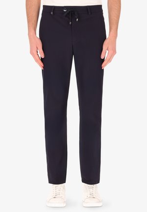 Pantaloni casual blu realizzati in tessuto leggero, caratterizzati da un cintura con lacci, vestibilità dritta e tasche frontali. Sneakers bianche completano il look.