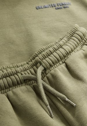 Joggebukser i olivengrønt bomuld med elastisk talje med rynket tekstur og snøre med metalender. "UNLIMITED FUNDAY" logo syet i gråt.
