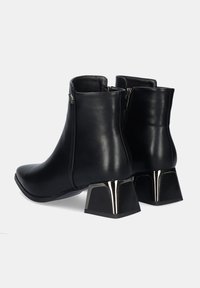 Botas de tobillo de cuero negro con tacones de bloque metálicos, con cremallera lateral y una textura suave y pulida. Diseño clásico.