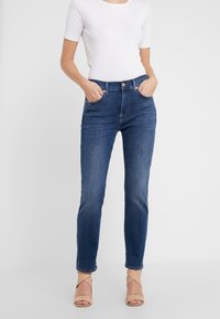 Tummansiniset korkeavyötäröiset farkut slim fit -mallilla, joissa on etutaskut, vyölenkit ja kevyt haalistuma. Yhdistetty tiukasti istuvaan valkoiseen paitaan.