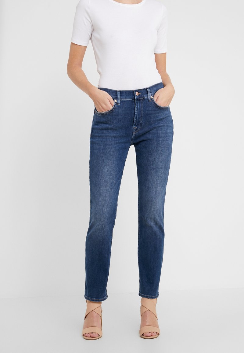 Tummansiniset korkeavyötäröiset farkut slim fit -mallilla, joissa on etutaskut, vyölenkit ja kevyt haalistuma. Yhdistetty tiukasti istuvaan valkoiseen paitaan.