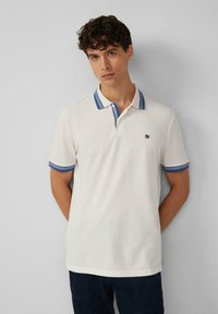 Polo shirt in off-white katoen met blauwe gestreepte kraag en mouwdetails. Voorzijde met logo, klassieke pasvorm, korte mouwen en knoopsluiting.