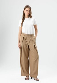 White crew-neck t-shirt, beige wide-leg trousers with front pleats, and black heeled sandals. Smooth fabric texture, relaxed fit.