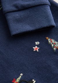 Polo in blu navy con alberi di Natale ricamati, stelle e accenti. Tessuto strutturato con colletto pieghevole e polsini a coste.
