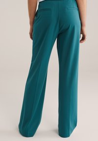 Široké nohavice tyrkysovej farby z hladkej látky, s dvoma zadnými vreckami a upraveným pásom, s čistým a jednoduchým dizajnom.