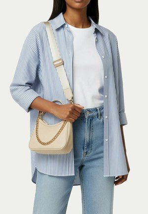 Žena v modrobíle pruhované košili na knoflíky přes bílé tričko, světlé modré džíny, drží béžovou kabelku se zlatým řetízkovým popruhem.