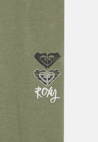 Alyvų žalios spalvos marškinėliai su tekstūruotu grafiniu širdelių raštu juoda ir balta spalvomis, su prekės ženklu "Roxy" ranka rašytu stiliumi.