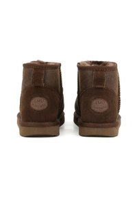 Stivali alla caviglia in suede marrone con fodera in shearling, suole in gomma piatta e logo EMU Australia impresso sul tallone. Design semplice e funzionale.