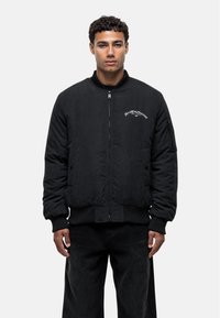 Giacca bomber nera realizzata in materiale morbido, con zip frontale, polsini e orlo a costine, e logo ricamato sul petto.