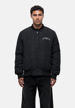 Veste bomber noire en matériau doux, dotée d'une fermeture éclair sur le devant, de poignets et d'un ourlet côtelés, et d'un logo brodé sur la poitrine.