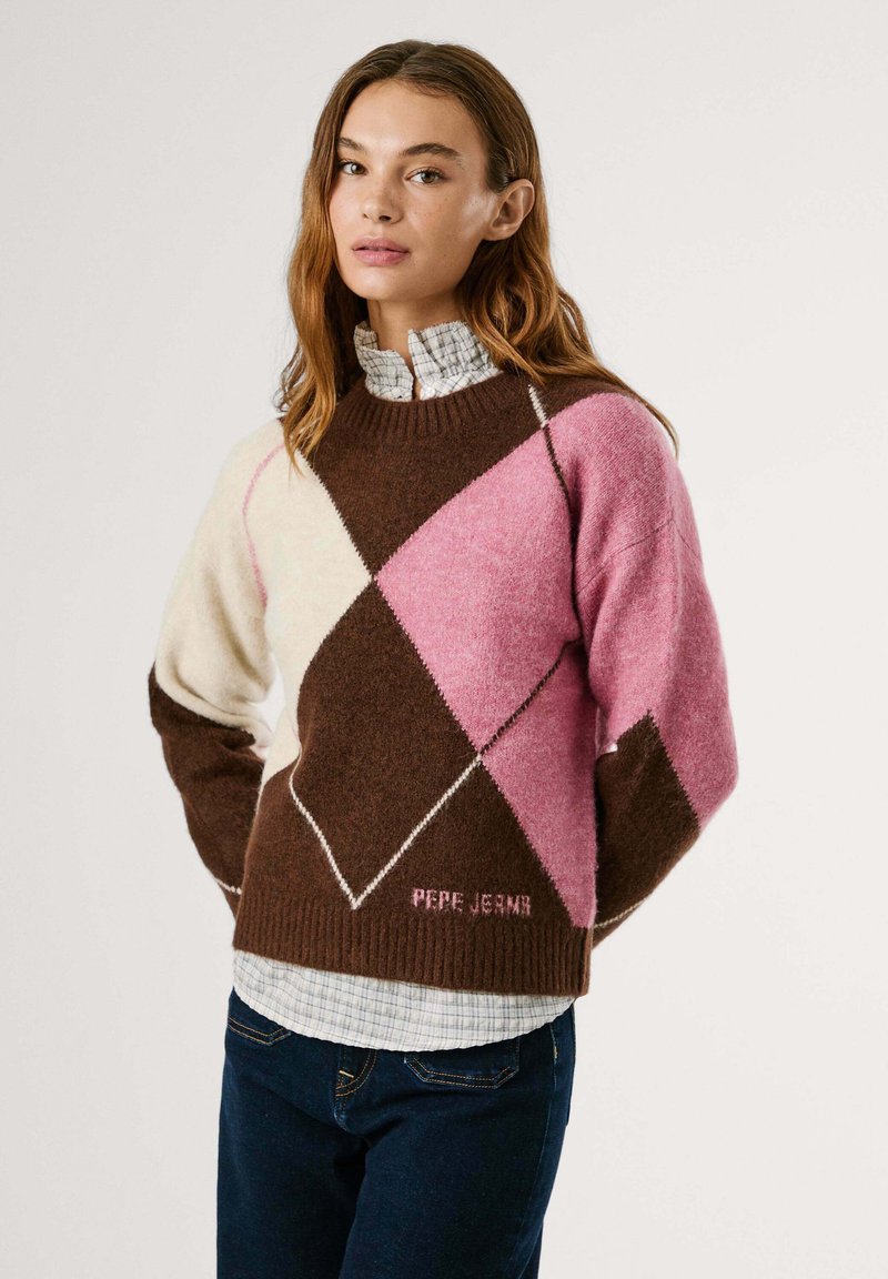 Färgglad stickad tröja med ett diamantmönster i bruna, rosa och krämiga nyanser. Ribbad halskrage och logotyp vid fållen. Lagd över en rutig skjorta.