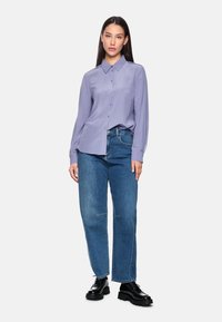 Light purple button-up shirt with long sleeves, paired with loose blue denim jeans and black lace-up shoes. Simple, modern design.