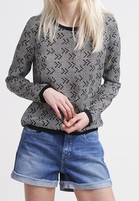 Pull noir et blanc à motifs avec des manches longues, un col rond et des poignets côtelés, associé à un short en denim bleu à ourlet retourné.