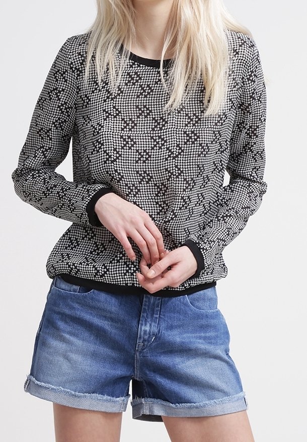 Pull noir et blanc à motifs avec des manches longues, un col rond et des poignets côtelés, associé à un short en denim bleu à ourlet retourné.