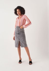 Camicia a righe rosa e bianca, abbinata a una gonna in denim grigia alta in vita con uno spacco frontale e dettagli sulle tasche. Mules nere con punta aperta.