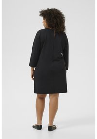 Robe noire �à manches trois-quarts, coupe droite, avec un décolleté au dos. Tissu lisse et design simple et minimaliste.