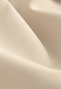 Béžová tkanina s hladkým, texturovaným povrchem. Materiál je lehký a má jemné, jednotné vzory tkaní.